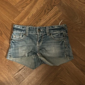 Blå jeansshorts från FB Sister - Snygga blå jeansshorts från FB Sister med slitna detaljer och råa kanter. Klassisk femficksmodell med kontrastsömmar och knappstängning framtill. Perfekta för varma dagar och en avslappnad look.