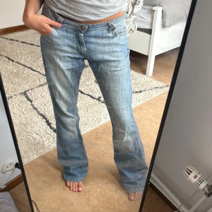 Ljusblå bootcut jeans från Lee - Säljer ett par ljusblå jeans från Lee med bootcut passform och låg midja. Jeansen har klassiska fem fickor, dragkedja och knapp framtill samt snygga slitningar för en avslappnad look. Perfekta för dig som gillar retrovibbar och bekväm stil.