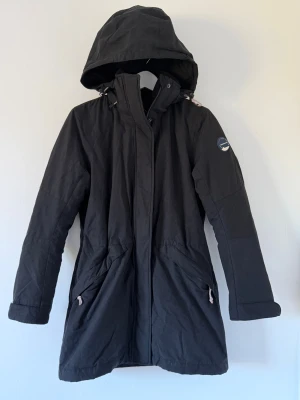 Svart jacka Peak Performance S - Svart parkajacka från Peak Performance i storlek S. Jackan har huva med snörning, två fickor med dragkedja och ett snyggt märke på ärmen. Insidan är quiltad och jackan är tillverkad i polyester, perfekt för kyliga dagar. Jackan gör att göra till två jackar beroende på väder 