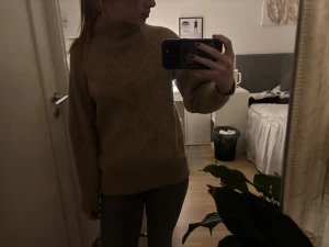 Beige stickad polotröja - Säljer en beige stickad polotröja med ribbad struktur och hög krage. Tröjan har långärmade och en loose passform som ger en chill och avslappnad vibe. Perfekt för att hålla sig varm under kyliga dagar.
