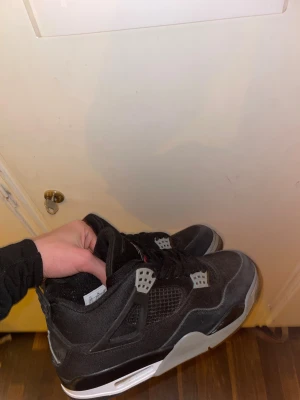 Svarta Nike Jordan 4 sneakers - Säljer ett par svarta Nike Jordan 4 sneakers med coola grå och vita detaljer. Skorna har meshpaneler, snörning och Jumpman-logga på både plös och häl. Snygg platt sula och klassisk rund tå. Perfekta för dig som gillar streetwear och vill sticka ut. Dom passar som 43