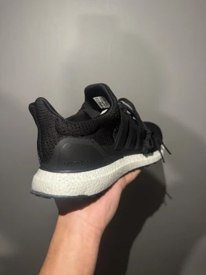 Adidas Ultraboost svarta sneakers - Svarta Adidas Ultraboost sneakers med stickad ovandel och vit Boost-sula. Skorna har snörning och en rund tå, samt diskret Adidas-logga på plösen. Perfekt för dig som gillar stilrena och bekväma sneakers med grym dämpning.