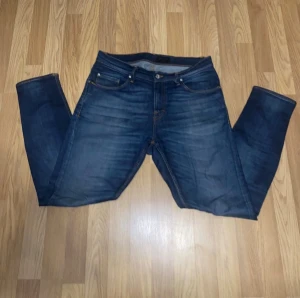 Tiger of Sweden mörkblå jeans - Snygga mörkblå jeans från Tiger of Sweden med klassisk femficksdesign och kontrastsömmar. Jeansen har en rak passform och är tillverkade i slitstarkt denim med läderpatch bak i midjan. Perfekta för dig som gillar stilrena och tidlösa jeans. Snabb affär 129kr annars 199kr