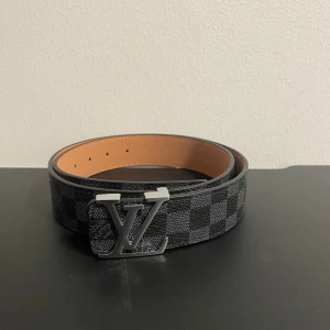  rutig svart skärp - Säljer ett bälte med spänne i silver. Bältet har ett rutigt mönster i svart och grått, och är tillverkat i skinn med beige insida. Perfekt accessoar för att lyfta din outfit med lyxig känsla och stil.