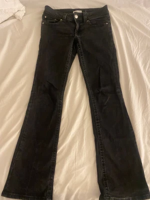 Svarta bootcut jeans från Gina Tricot  - Svarta jeans från Gina Tricot i bootcut-modell med låg midja. Klassisk femficksdesign med snygga detaljer på bakfickorna och silverfärgade knappar. 