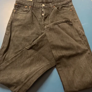 Levi's 501 svarta jeans - Svarta Levi's 501 jeans med klassisk knappgylf och raka ben. Jeansen har fem fickor och är tillverkade i slitstarkt denimtyg. Perfekt för dig som gillar tidlös stil och vill ha ett par jeans som funkar till allt.