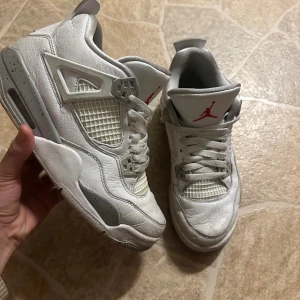 Nike Air Jordan 4 Retro vit/grå ÄKTA - Nike Air Jordan 4 Retro sneakers i vit och grått med röda detaljer. Skorna har snörning, platt sula och meshpaneler på sidorna. Ikonisk Jumpman-logga på plösen och undersidan. Tillverkade i skinn och syntetmaterial, med rund tå och coola plastdetaljer. De är ÄKTA!