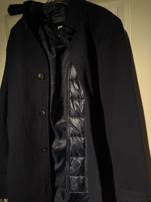 Mörkblå rock  - Marinblå kappa  från Strömberg med stilren design och  kappan  har klassisk krage med spänne, knäppning framtill men också avtagbar dragkedja. Perfekt för dig som vill ha en snygg och varm kappa  med lite extra edge under höst och vinter.