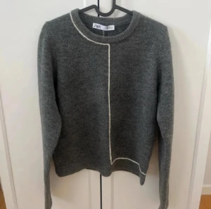 Grå stickad tröja från Zara - Snygg grå stickad tröja från Zara med vit kontrastsöm som går längs halsen och ner över framsidan och baksidan. Den passar även för dom som har xs och s efter som jag har de i alla mina kläder och denna tröja passar mig. 🥰