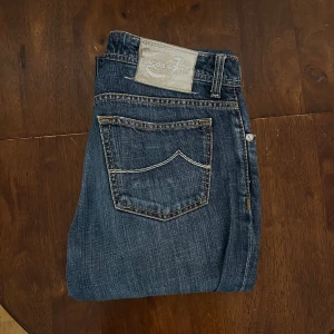 Jacob Cohen jeans - Snygga blå jeans från Jacob Cohen med klassisk femficksdesign, kontrastsömmar och broderad logga på myntfickan. Modell J688 som är en slim fit modell. Nypris på liknande är runt 4-5000 kr.  Jeansen är använda men har inga tydliga defekter. Size 33. Midja: ca 43 cm. Längd från midja: 110 cm. Längd från gren : 84 cm. Perfekta för dig som gillar stilrena och tidlösa jeans. Kom med bud