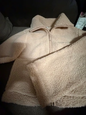 Beige teddyjacka från H&M XS - Mysig teddyjacka från H&M i beige färg, storlek XS. Jackan har en hög krage och dragkedja framtill. Tillverkad i fluffigt syntetmaterial som ger en cool och avslappnad vibe. Perfekt för kyliga dagar och enkel att matcha med jeans eller mjukis.