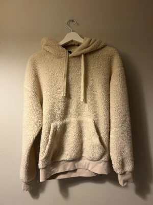 Beige teddy hoodie Jack & Jones - Mysig beige teddy hoodie från Jack & Jones med huva och snörning. Tröjan har en stor magficka och ribbade muddar vid ärmslut och nederkant. Perfekt för kalla dagar när du vill vara extra comfy och chill.