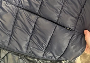 Mörkblå pufferjacka från Vero Moda - Snygg mörkblå pufferjacka från Vero Moda med raka kanaler och dragkedja framtill. Jackan har lång ärm och en clean, stilren look som funkar till många outfits. Materialet är syntet och jackan är lätt vadderad för extra värme.