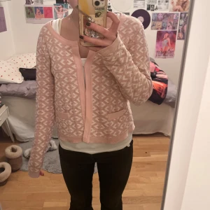 Ljusrosa mönstrad kofta - Superfin ljusrosa kofta med vitt geometriskt mönster och två små fickor fram. Koftan har hakar som stängning och är långärmad med rund hals. Den är hyfsat kort och vid i passformen. Precis köpt på Vinted för 50 kr, inget angett märke, har själv aldrig använt och i gott skick från tidigare säljare. Sitter som en XS/S🤍🤍