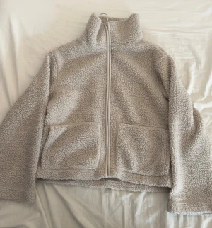 Beige teddyjacka från 157, storlek S - Mysig beige teddyjacka från 157 med hög krage och två stora fickor framtill. Jackan har hel dragkedja och är tillverkad i fluffigt fleece-material.