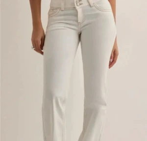 Vita jeans Nelly storlek 34/xs - Snygga vita jeans från Nelly med bootcut passform och hög midja. Jeansen har klassiska fem fickor, kontrastsömmar och coola broderade detaljer på bakfickorna. Tillverkade i stretchig bomull för skön passform och stilren look.