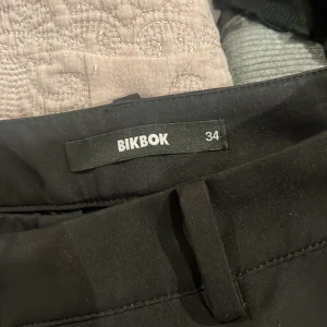 Svarta kostymbyxor från Bik Bok - Snygga svarta kostymbyxor från Bik Bok i storlek 34. Byxorna har klassisk rak passform med hällor för bälte och diskret front. Högmidjade Perfekta för en clean och stilren look, passar till både sneakers och boots.