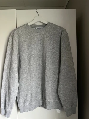 Grå sweatshirt från Weekday - En stilren grå sweatshirt från Weekday i storlek S. Tröjan har rund hals och ribbade muddar vid ärmslut. Perfekt för chill dagar och enkel att matcha med jeans eller joggers.