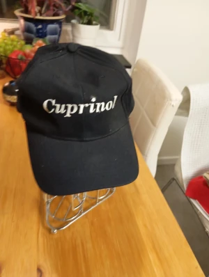 Svart keps med Cuprinol-tryck - Svart keps med böjd skärm och vit broderad text 'Cuprinol' framtill. Klassisk modell med justerbar passform bak. Perfekt för dig som gillar enkel och stilren streetwear.