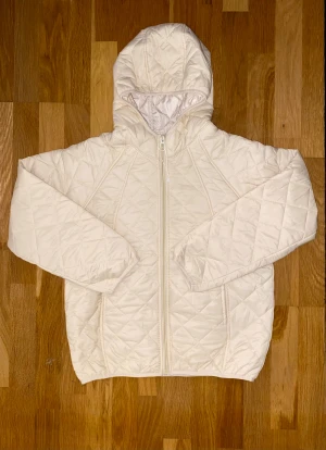 Vit quiltad pufferjacka med huva - Säljer en vit pufferjacka med quiltat mönster och huva. Jackan har dragkedja framtill och är långärmad med elastiska muddar. Perfekt för kyliga dagar och har en clean, stilren look som funkar till många outfits.