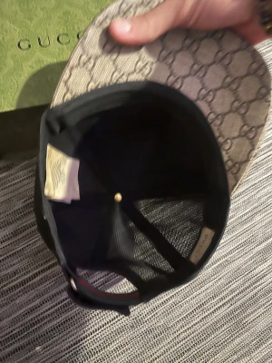 Gucci keps med tigertryck - Snygg keps från Gucci med klassiskt GG-mönster i beige och brunt, prydd med två coola tigrar framtill. Baksidan är i svart mesh och kepsen har justerbar rem. Perfekt för dig som vill sticka ut med lyxig streetstyle. Den är använd men funkar bra, är inte sönder någon stans. Du får box och dustbag och kvitto skickas genom bild eftersom den köptes online.