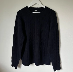 Mörkblå kabelstickad tröja från Uniqlo - Mörkblå kabelstickad tröja från Uniqlo i storlek S. Tröjan har rund hals och långärmade ärmar. Materialet är en mix av akryl, återvunnen polyester, ull och elastan vilket gör den både mjuk och varm. Perfekt för dig som gillar klassisk stil med lite struktur. 4Ö1