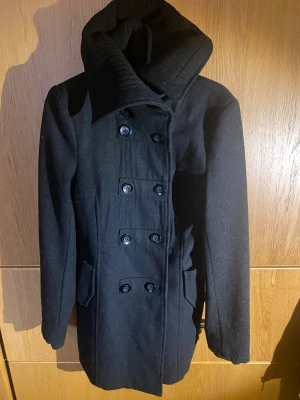 Svart skepparkavaj från ONLY XS - Säljer en svart skepparkavaj från ONLY i storlek XS. Jackan har dubbelknäppning med stora svarta knappar, bred ribbad krage och fickor med lock. Materialet är ullblandning som håller dig varm under kyliga dagar. Perfekt för dig som gillar klassisk stil med en twist.