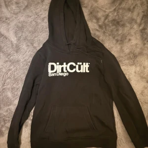 Svart hoodie från DirtCült - Säljer en svart hoodie från DirtCült med tryck 'San Diego' på framsidan. Den har en klassisk känguruficka. Perfekt för en avslappnad stil. Storlek XL men passar som S