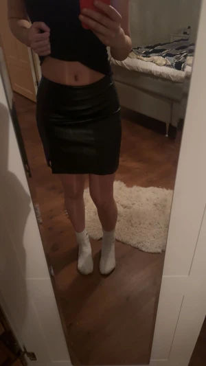 Svart kort kjol i skinn - Säljer en svart kort kjol i skinnimitation med tight passform. Kjolen har en slits på sidan som ger en snygg detalj och sitter högt i midjan. Perfekt för dig som gillar en edgy och stilren look. Skit snygg kjol som aldrig kommit till användning ‼️☺️