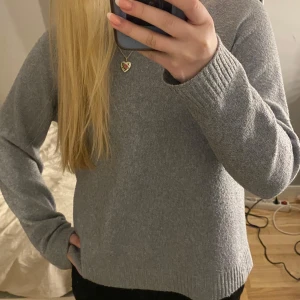 Grå stickad tröja - Mysig grå stickad tröja perfekt för kyligare dagar. Tröjan har en enkel design med långa ärmar och en bekväm passform. Perfekt för att hålla sig varm och stilren.
