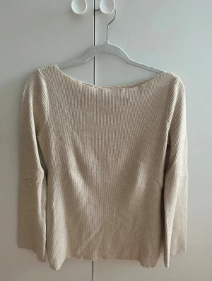 Beige ribbad tröja med omlott baktill - Supersnygg beige ribbad tröja med lång ärm och snygg omlottdetalj baktill. Perfekt för dig som gillar stilrena plagg med en tvist. Passar perfekt till både jeans och kjol
