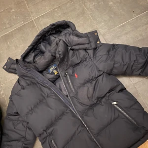 Marinblå puffer jacka från polo ralph lauren  - Mörkblå polo Ralph Lauren jacka, den är i bra skick men den ena fickan går inte att stänga annars är den i bra skick. Den är puffig och har en luva man kan ta av och på. Den är jättefin men har blivit lite för liten för mig. Original priset är 2000💞