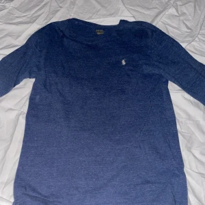 Blå långärmad tröja från Polo Ralph Lauren - Snygg marinblå långärmad tröja från Polo Ralph Lauren med klassisk rund hals och diskret broderad logga på bröstet. Perfekt för dig som gillar stilrena och enkla plagg. Mjuk bomullskvalitet som känns skön mot huden.
