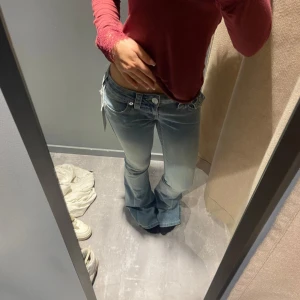 Ljusblå bootcut jeans låg midja - Säljer ett par ljusblå bootcut jeans med låg midja och snygg tvätt. Jeansen har klassiska fickor fram och bak, samt dragkedja och knapp i midjan. Materialet är jeans och passformen är loose nertill med utsvängda ben.true religion lite slitna där nere annars i bra kvalite, är 158 och dom är långa för mig fortfarande även om jag har rivit av lite så dom blir lite kortare