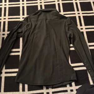 Mörkgrön skjorta från Luca Faloni - Snygg mörkgrön skjorta från Luca Faloni, tillverkad i Italien. Skjortan har klassisk krage, knappar framtill och långa ärmar. Materialet är mjukt och känns lyxigt, troligtvis linne. Perfekt för dig som gillar stilrena och tidlösa plagg.