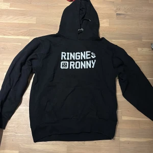 Svart hoodie Ringnes Ronny - Säljes då den endast legat i garderoben o samlat damm i flera år. Texten spruckit lite som de flesta gör med tiden. Inget som syns tydligt när man bär den.  Pris kan diskuteras, köparen står för frakten!! OBS! Tvättas innan!!
