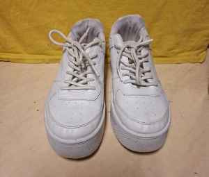 Vita sneakers med platt sula - Snygga vita sneakers med klassisk design och platt sula. Skorna har rund tå, snörning och perforerade detaljer på ovansidan för extra stil. Tillverkade i skinn med mjuk textil på insidan för skön komfort. Perfekta för dig som gillar en clean och enkel look.