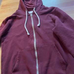 Vinröd hoodie från Pier One - Säljer en vinröd hoodie från Pier One med huva och vita snören. Tröjan har dragkedja framtill, två fickor och är tillverkad i mjuk bomull. Perfekt för chill dagar och enkel att matcha med jeans eller joggers. Jag är 160 cm lång och den passa fint när man viker in mudden( längst ner på tröjan). Hör av er vid funderingar! 