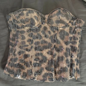 Leopardmönstrad paljettkorsett  - Säljer en snygg korsett från New Yorker i storlek XS med leopardmönster och glittriga paljetter över hela toppen. Korsetten har en beige bas, formade kupor och dragkedja i sidan för enkel påklädning. Aldrig använd, endast testad.