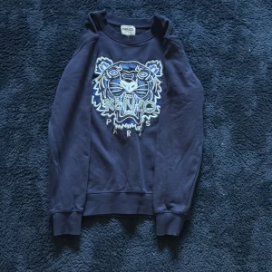 Mörkblå Kenzo sweatshirt med tiger - Snygg mörkblå sweatshirt från Kenzo Kids med ikonisk broderad tiger och Kenzo Paris-text på bröstet. Tröjan har långa ärmar, ribbade muddar och är gjord i mjuk bomull. Perfekt för dig som gillar statement-plagg och coola detaljer.