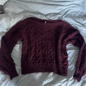Vinröd stickad tröja - Säljer en vinröd stickad tröja med snyggt kabelmönster och bred ribbad kant vid midja och ärmslut. Tröjan har långärmade ärmar och en rundad halsringning. Perfekt för dig som gillar mysiga och stilrena plagg med lite extra struktur. Den är pyttelite nopprig men knappt npgot man ser och har inte använts ett fåtal gånger