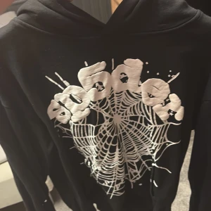 Svart hoodie med spindelnätsprint - Svart hoodie med stor vit spindelnätsgrafik och coolt tryck framtill. Tröjan har huva och långa ärmar, perfekt för dig som gillar streetstyle och vill sticka ut med ett unikt motiv.