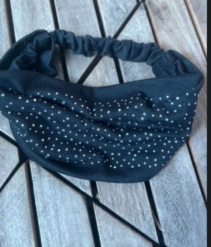 Svart diadem med prickigt mönster - Snyggt svart diadem med vita prickar som ger en cool och lekfull vibe. Diademet har en elastisk baksida för skön passform och är tillverkat i mjukt tyg, perfekt för att piffa upp din look.