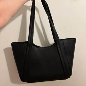 Svart axelväska från Even&Odd - Stilren svart axelväska från Even&Odd i syntetmaterial med två långa handtag och magnetlås. Väskan har en rymlig insida och enkel, modern design som passar perfekt till din vardagsstil.