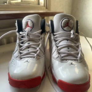 Nike Air Jordan 6 Rings vit/röd US 7Y - Nike Air Jordan 6 Rings sneakers i vit och röd färg med svart och gråa detaljer. Skorna har snörning, rund tå och platt sula. Materialet är en mix av syntet och mesh, med Jumpman-logga på plösen och hälen. Perfekt för dig som gillar klassiska basketinspirerade sneakers.