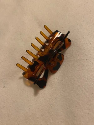 Hårklämma - brun genomskinlig med svarta fläckar - Säljer en snygg hårklämma i brun genomskinlig plast med svarta fläckar. Knappt använd och i superfint skick!  Perfekt för att hålla håret på plats med stil, passar både vardag och fest. Frakt kan tillkomma.