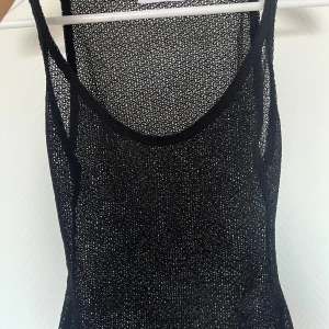 Svart stickad ärmlös klänning - Snygg svart stickad linne  med rundad halsringning. Materialet är genomskinligt och ger en cool mesh-effekt, perfekt för att skapa en edgy look. Passar dig som gillar att sticka ut och vill ha något unikt i garderoben. (Aldrig använd)