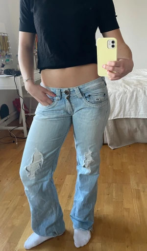Ljusblå slitna jeans från Pepe Jeans - Säljer ett par ljusblå jeans från Pepe Jeans med slitningar på knäna och fransig nederkant. Modellen har låg midja, raka ben och klassiska fem fickor. Jeansen är tillverkade i mjukt denim och har en avslappnad passform. 