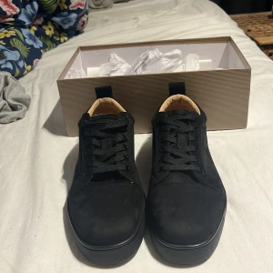 Svarta sneakers från Christian Louboutin - Snygga svarta sneakers från Christian Louboutin med klassisk röd sula och diskret logga på insidan. Skorna har rund tå, snörning och är tillverkade i mocka med beige innersula. Perfekt för dig som vill ha en lyxig och stilren look.priset kan såklart sänkas vid snabb affär 