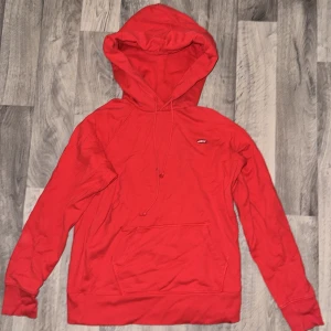 Röd hoodie från Levi's med huva - Snygg röd hoodie från Levi's med klassisk logga på bröstet. Tröjan har huva med snörning och en stor magficka framtill. Tillverkad i mjuk bomull och har långa ärmar. Perfekt för chill dagar och streetstyle. Storlek kan passa från XS-S- mindre M jag är 181 cm